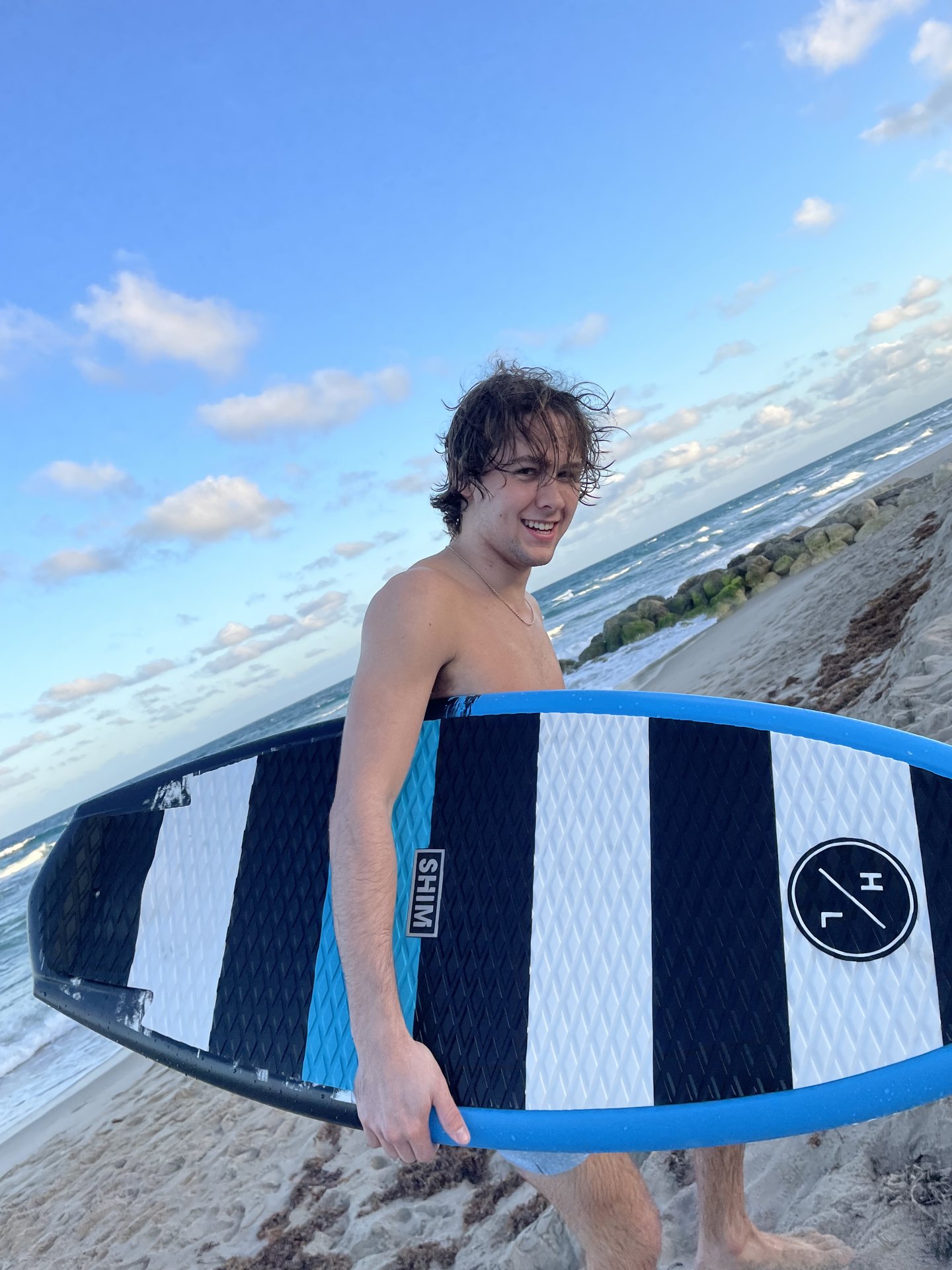 Derwin Hauser walking on beach carrying surfboard
