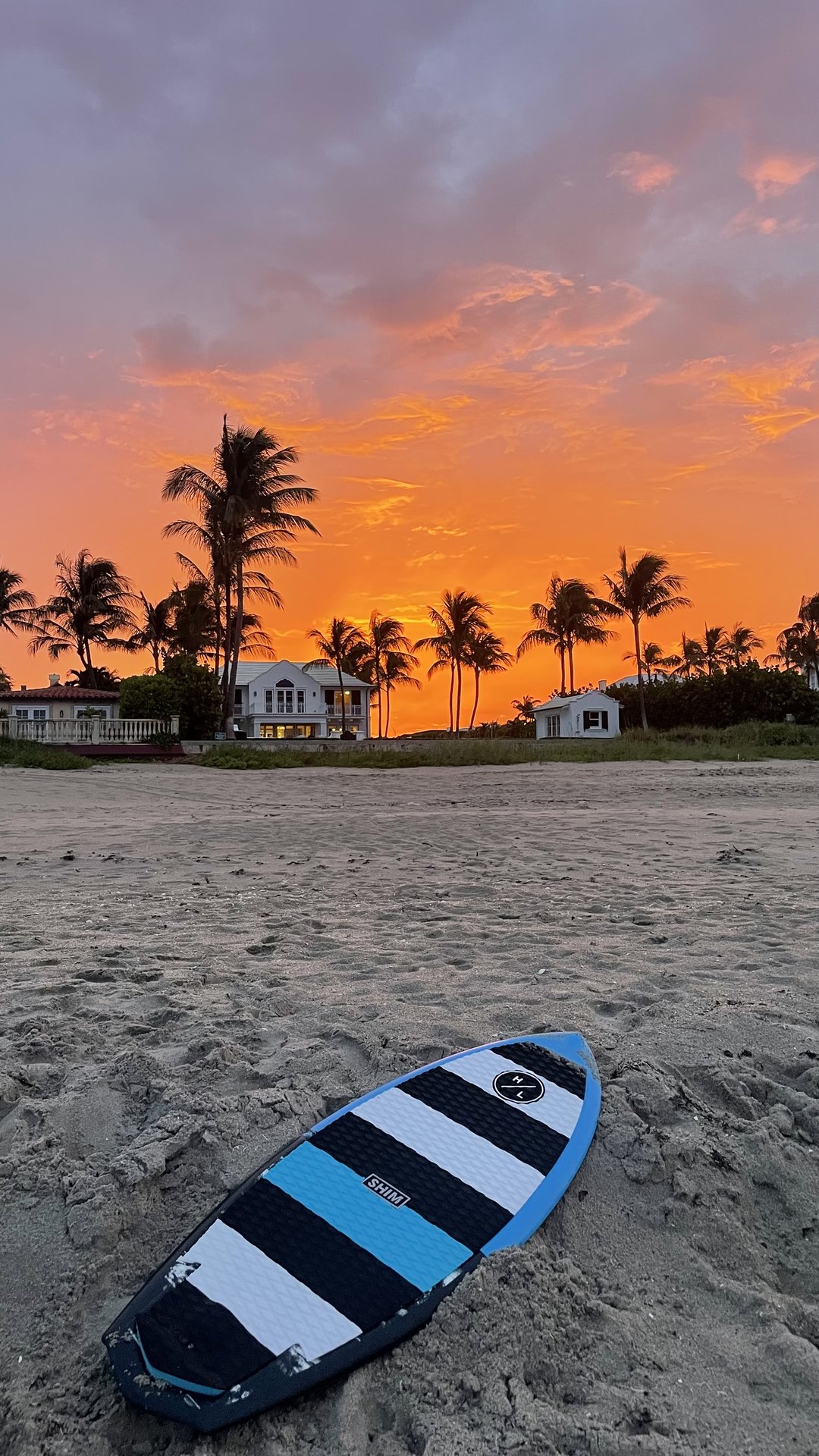 surfboard on beach with sunset in the background